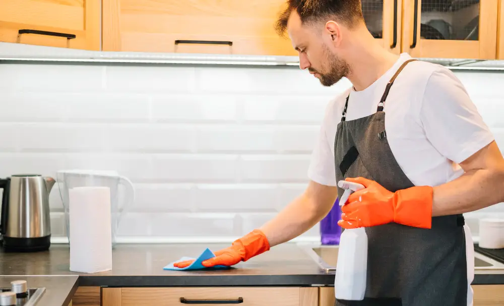 Domestic cleaner wiping kitchen worktops with a cloth and spray in a London home
